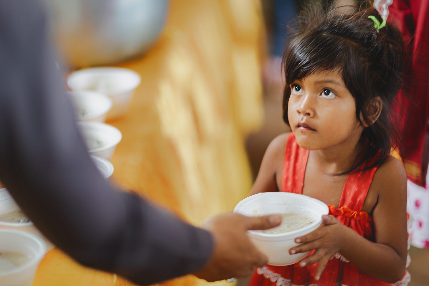 A Cambodian child receiving food from a police officer at a temporary refugee centre at the Thai/Cambodia border. © Gavin Gough