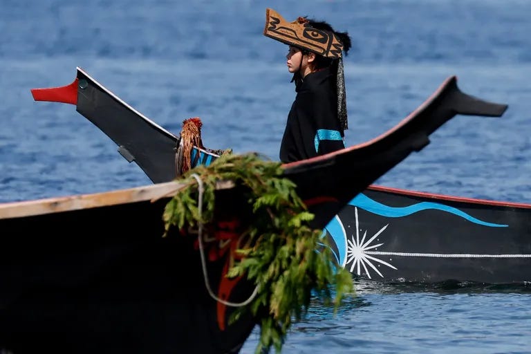 A canoe from the Tulalip people comes into the beach with a young member dressed in traditional regalia in the bow. (Jennifer Buchanan / The Seattle Times)