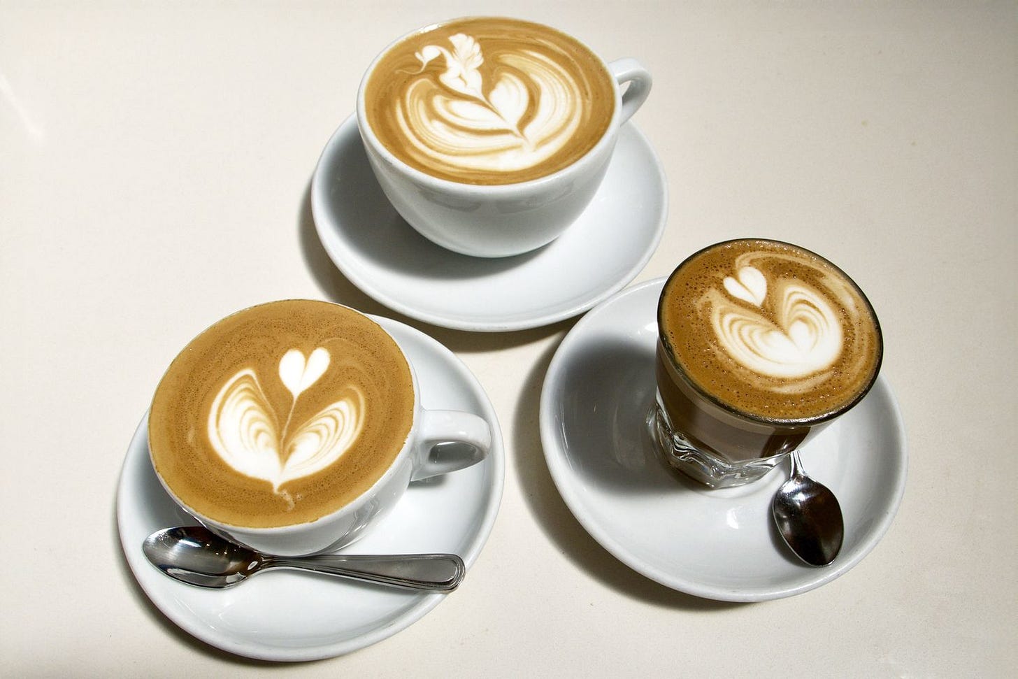 Three cups of coffee featuring steamed milk latte art designs on top, showcasing barista techniques