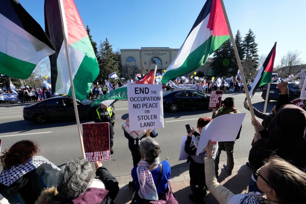 People protest on different parts of the street waving Palestine and Israel flags. Multiple signs are held, including a main one that says "END THE OCCUPATION NO PEACE ON STOLEN LAND!"