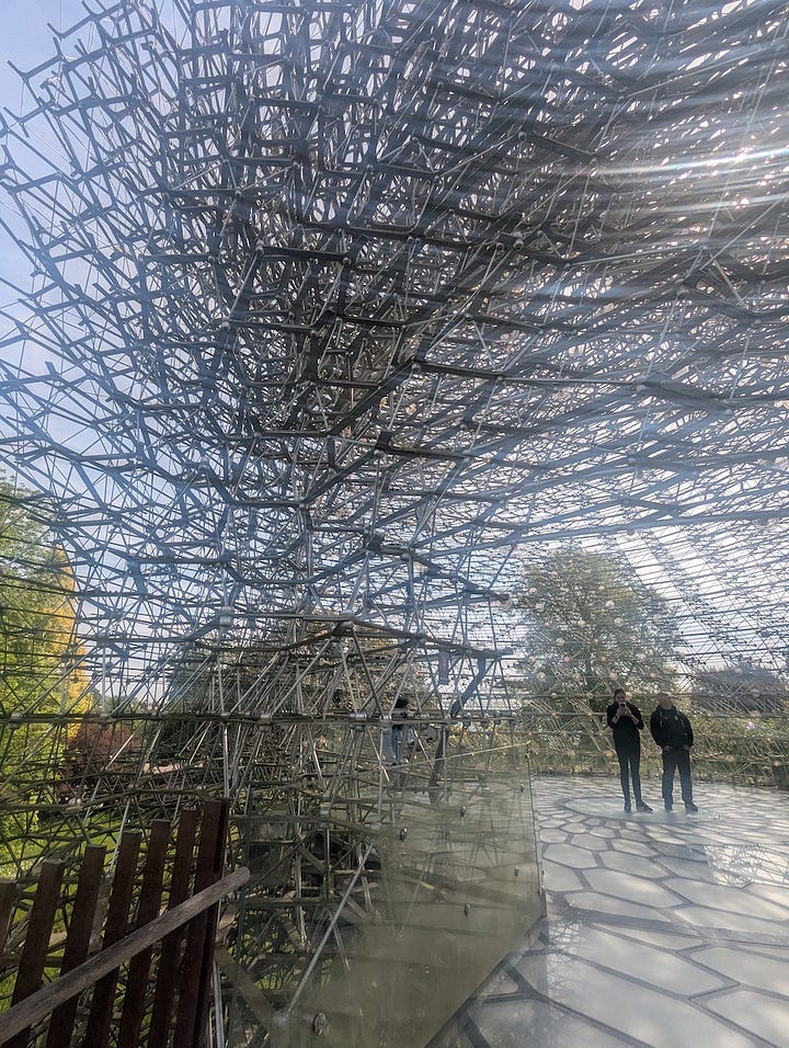 Three views of The Hive at Kew Gardens, a large aluminium lattice structure rising from a grassy landscape, shown from a distance, from beneath, and looking up through its circular interior.