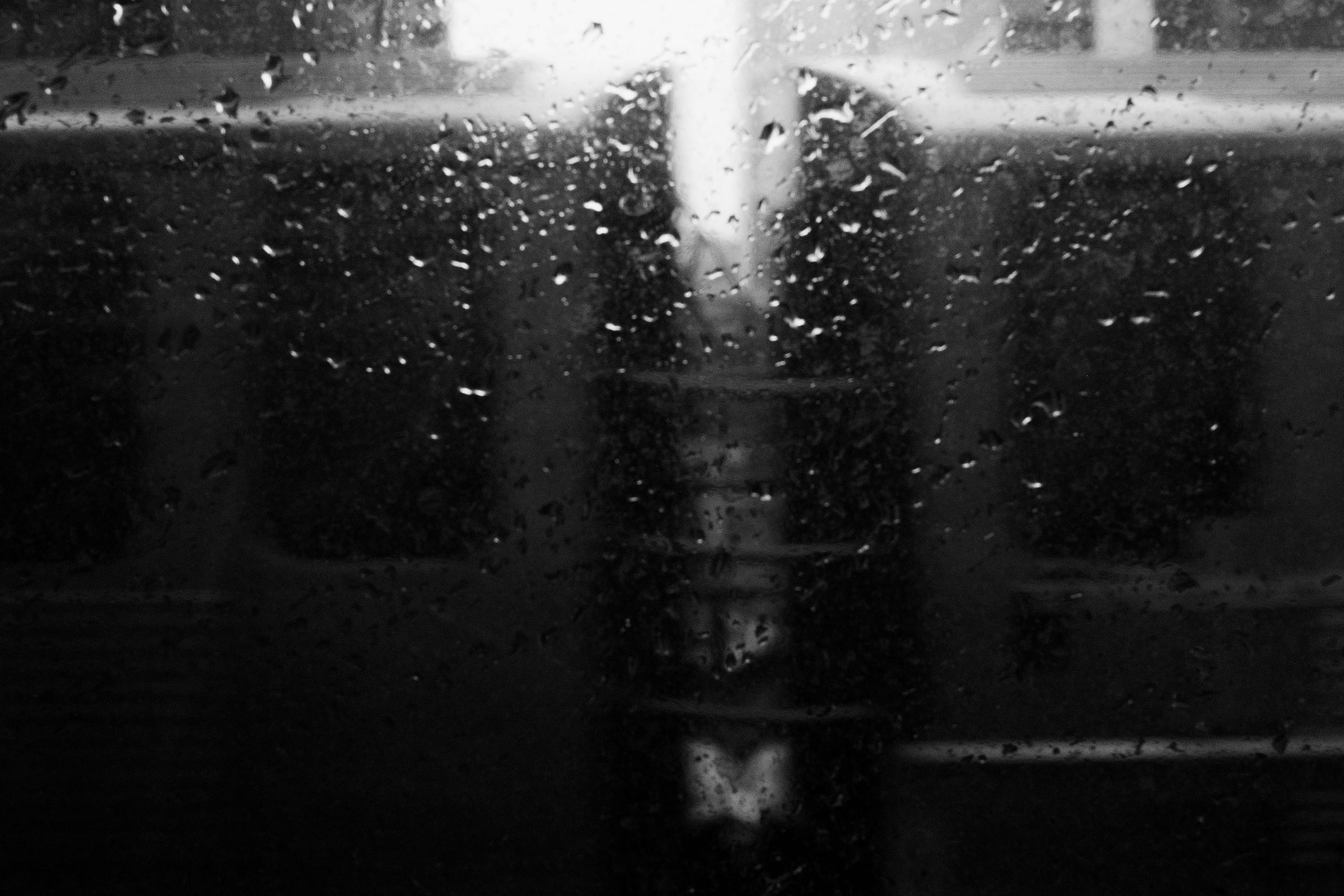 Rain-covered window blurring the view of a train stopped at the platform, with a bright light shining through the gap between the train cars. Rain-covered window blurring the view of a train stopped at the platform, with a bright light shining through the gap between the train cars.
