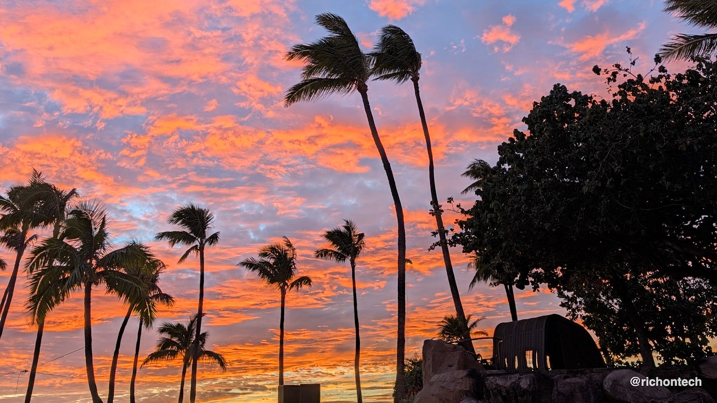 Palm trees silhouetted against a vivid orange, pink and purple sunset sky in Maui.