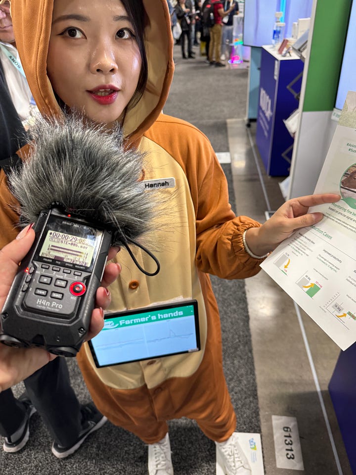 A super futuristic electric motorcycle, a woman in a cow suit being interviewed by me, and conference signs touting carbon capture, battery technology, and spray to extend food shelf life.