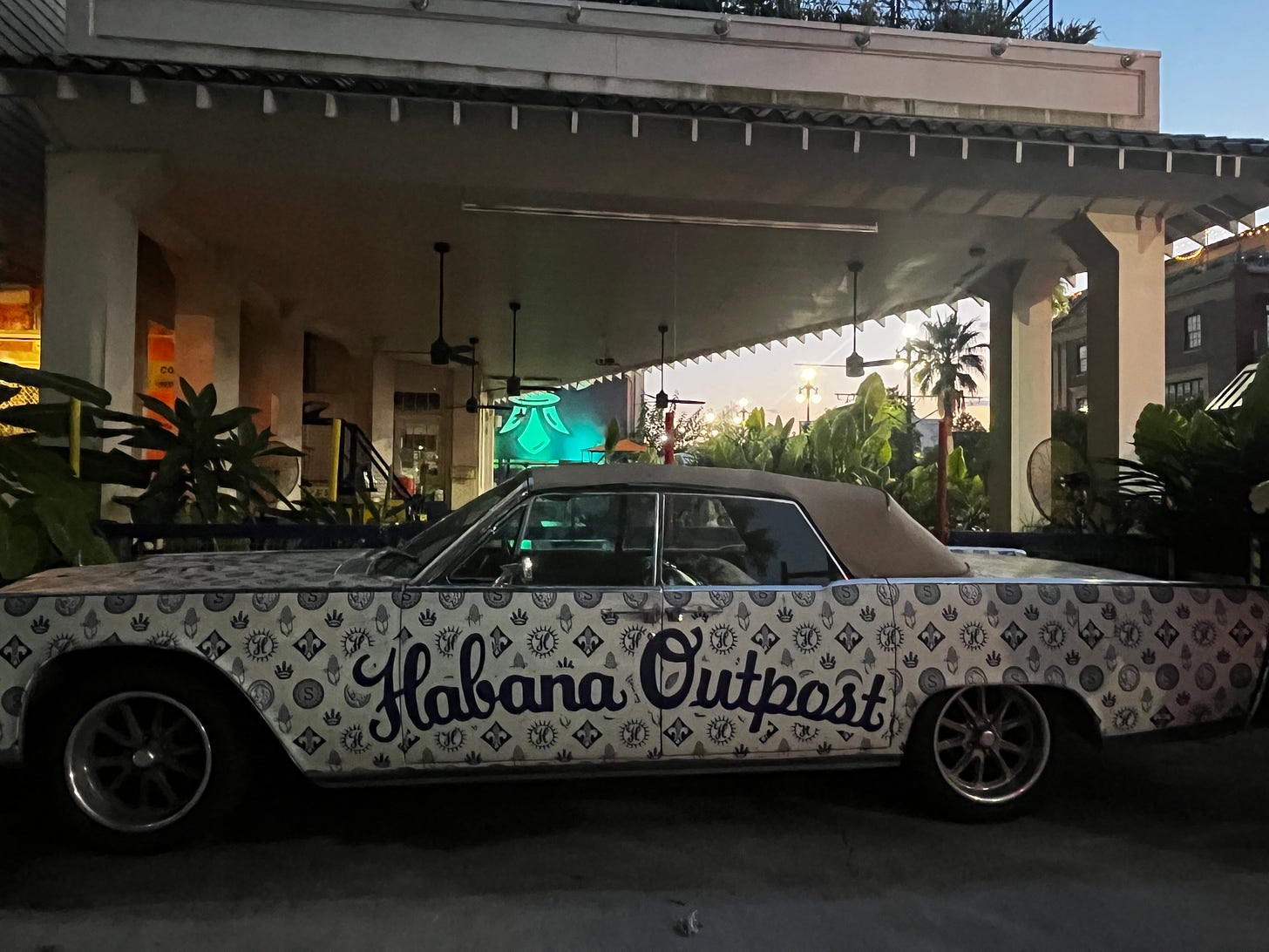 The exterior of Habana Outpost in New Orleans. An older car is wrapped in decorative wrapping with Habana Outpost written across the doors. 
