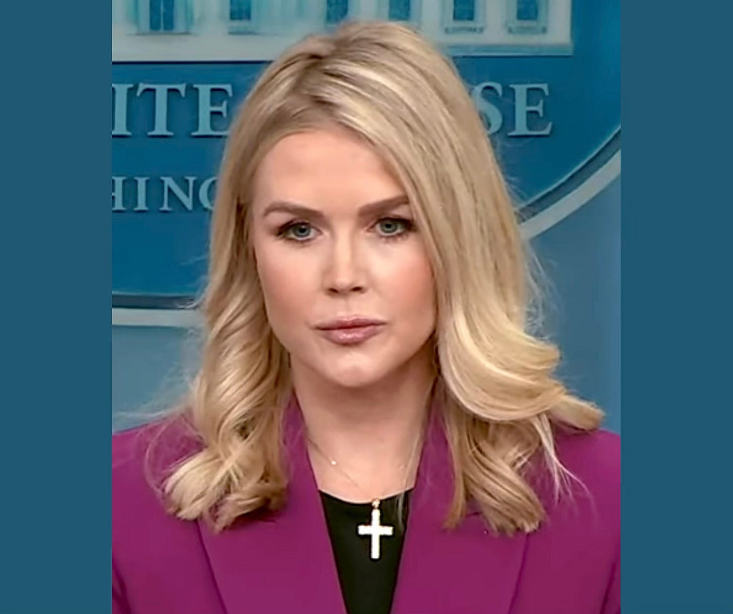 Young blonde woman stands at podium, wearing a hot pink suit and a large cross of 2 1/2 or 3 inches in length around her neck. The White House, Washington, D.C. is emblazoned on the wall behind her. She is staring at someone behind the camera, wearing a scowl on her face. Young blonde woman stands at podium, wearing a hot pink suit and a large cross of 2 1/2 or 3 inches in length around her neck. The White House, Washington, D.C. is emblazoned on the wall behind her. She is staring at someone behind the camera, wearing a scowl on her face.