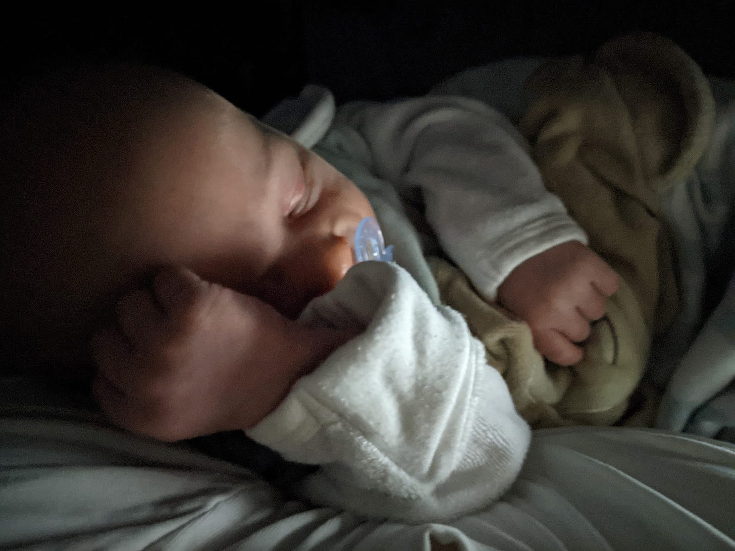 sleeping baby in the dark with a blue dummy