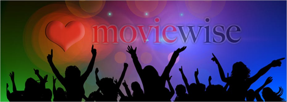 A crowd of people with their arms up in the air cheer happily in a darkened concert hall.