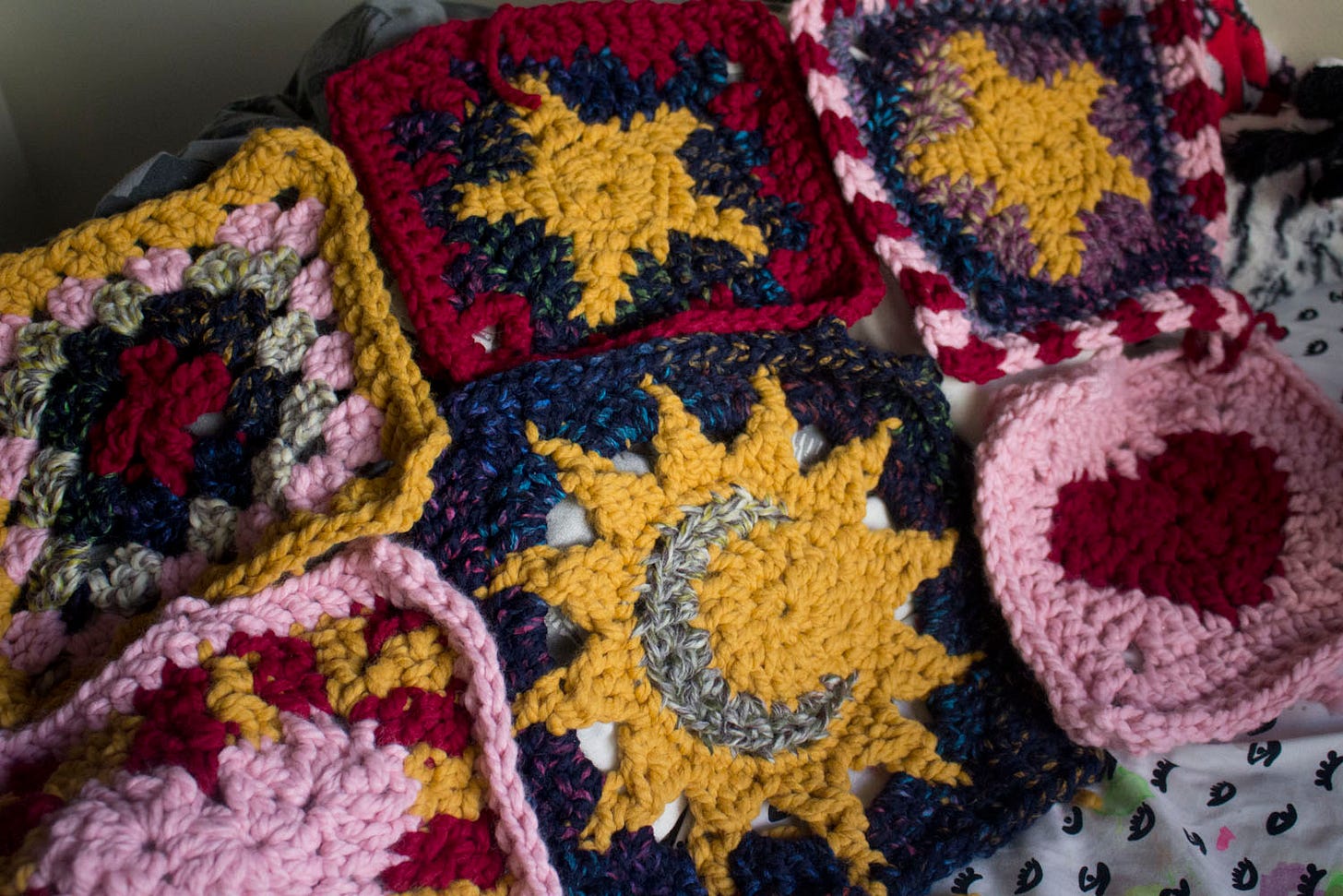 several large crocheted squares in red, pink, yellow, and blue. they have celestial and heart motifs