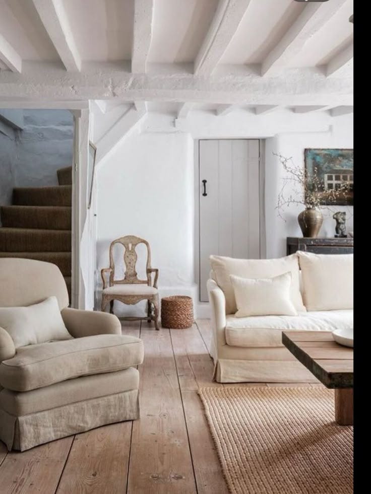 This may contain: a living room with white walls and wooden floors is pictured in this image, there are two couches on the far side of the room