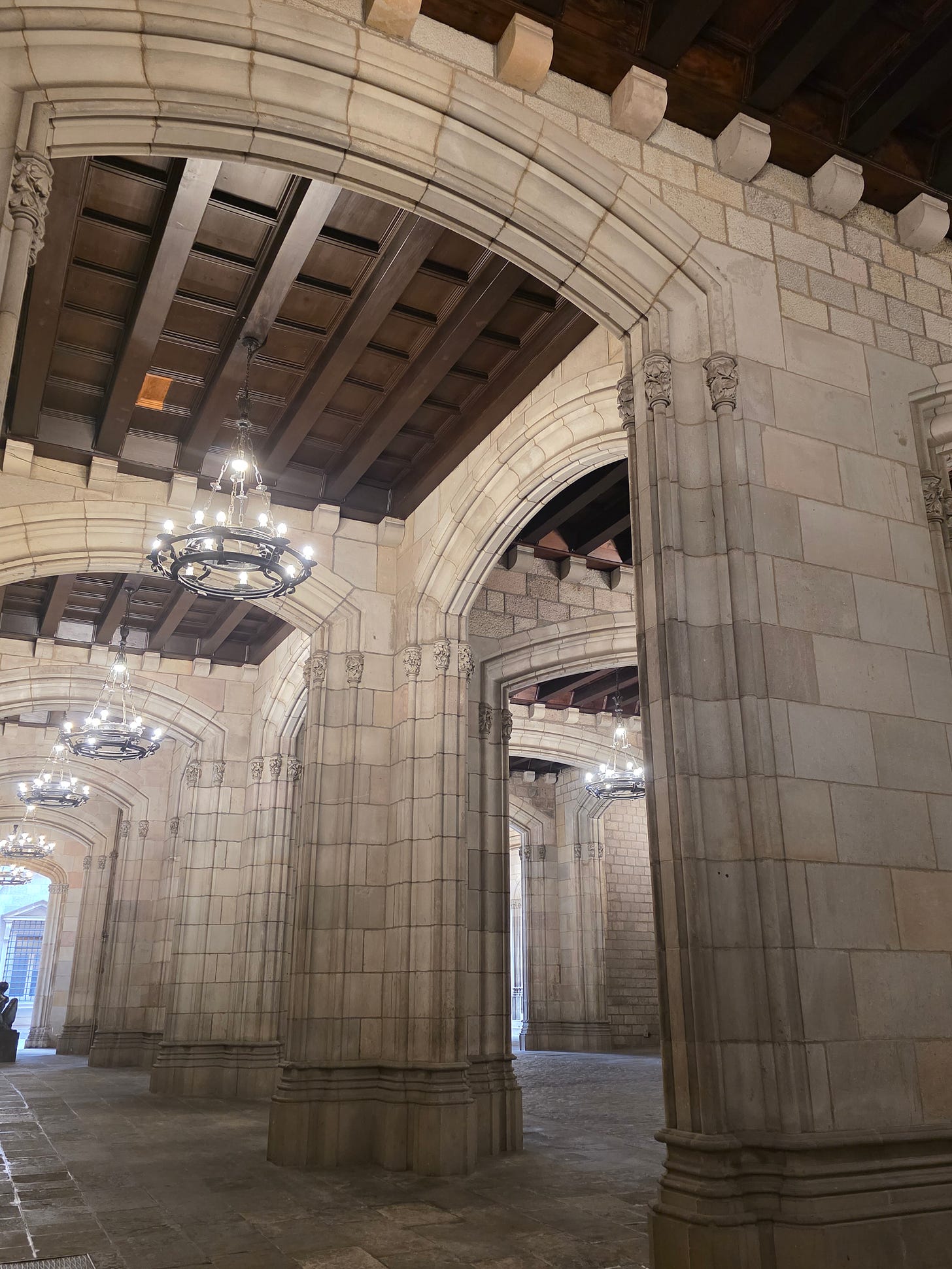 Arcos de piedra góticos y grandes lámparas colgantes en el patio interior del Ayuntamiento de Barcelona.