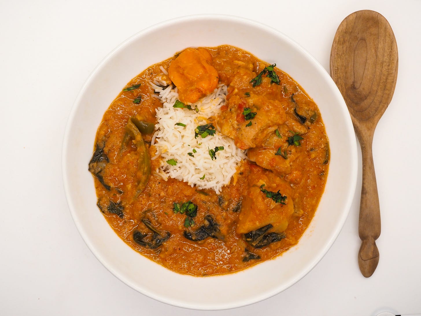 A bowl of chicken maafe (in peanut sauce) with basmati rice in the middle of the bowl. A wooden spoon is next to the bowl.