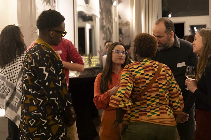 Two photos. The left-hand photo shows a group of 6 people gathered around a large table doing arts & crafts on a flowery table cover, surrounded by paints. The right-hand photo shows a group of three people talking at an event. A woman with long brown hair and glasses is listening to another participant with their back turned wearing a checked yellow shirt. A third person in a brown patterned jacket and glasses is listening.