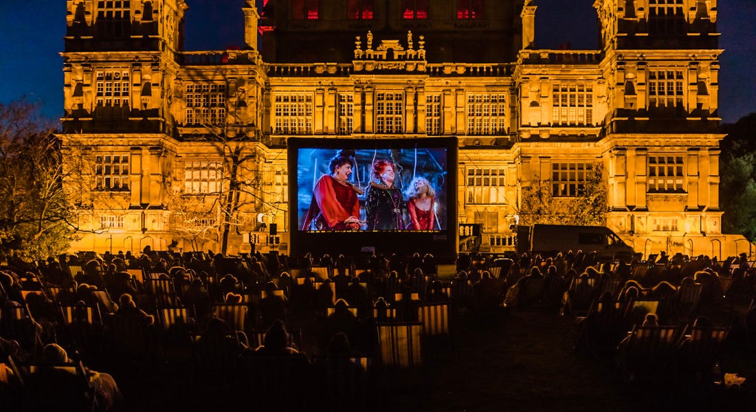 An evening at Wollaton Hall with the building lit up, a cinema screen in front of it, and a group of people in deckchairs in front of it An evening at Wollaton Hall with the building lit up, a cinema screen in front of it, and a group of people in deckchairs in front of it