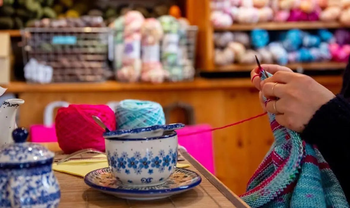 hands knitting and cup of tea on a table surronded by yarn