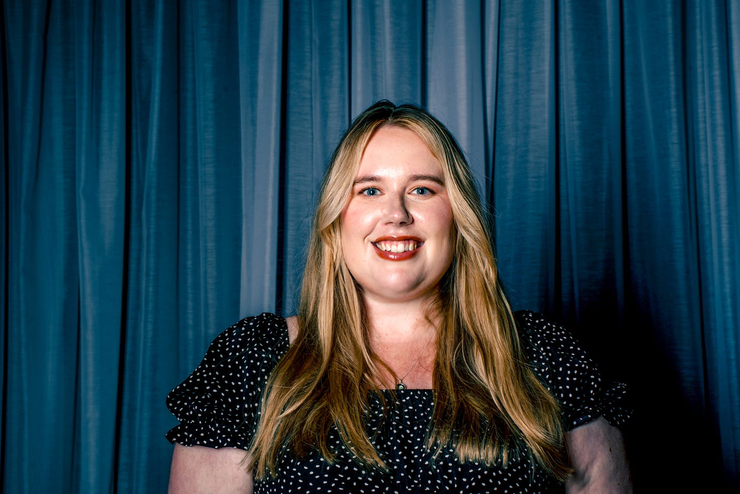 Headshot of MG Hunt. She faces the camera with a blue curtain background behind. Headshot of MG Hunt. She faces the camera with a blue curtain background behind.