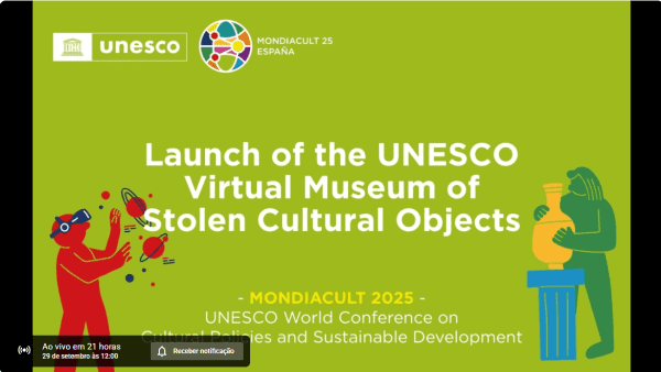 #descrevemospravocê  O card anuncia o lançamento do Museu Virtual da UNESCO de Objetos Culturais Roubados. O texto em inglês informa: Launch of the UNESCO Virtual Museum of Stolen Cultural Objects – Mondiacult 2025 – UNESCO World Conference on Cultural Policies and Sustainable Development. No canto superior esquerdo está o logotipo da UNESCO, e no direito, o selo circular da Mondiacult 25, com a palavra España logo abaixo.  O fundo é verde, e a composição traz duas ilustrações estilizadas em cores vivas. À esquerda, uma figura humana em vermelho, com óculos azuis, segura uma câmera e parece registrar a cena, com traços em preto e amarelo representando flashes ou movimento. À direita, uma figura em verde segura um vaso dourado em estilo antigo, colocado sobre uma pequena coluna azul, sugerindo um objeto de valor cultural.  Na parte inferior esquerda, aparece uma caixa preta típica de plataformas de vídeo ao vivo, indicando a transmissão futura: “Ao vivo em 21 horas, 29 de setembro às 12:00”, acompanhada de um botão branco escrito “Receber notificação”.
