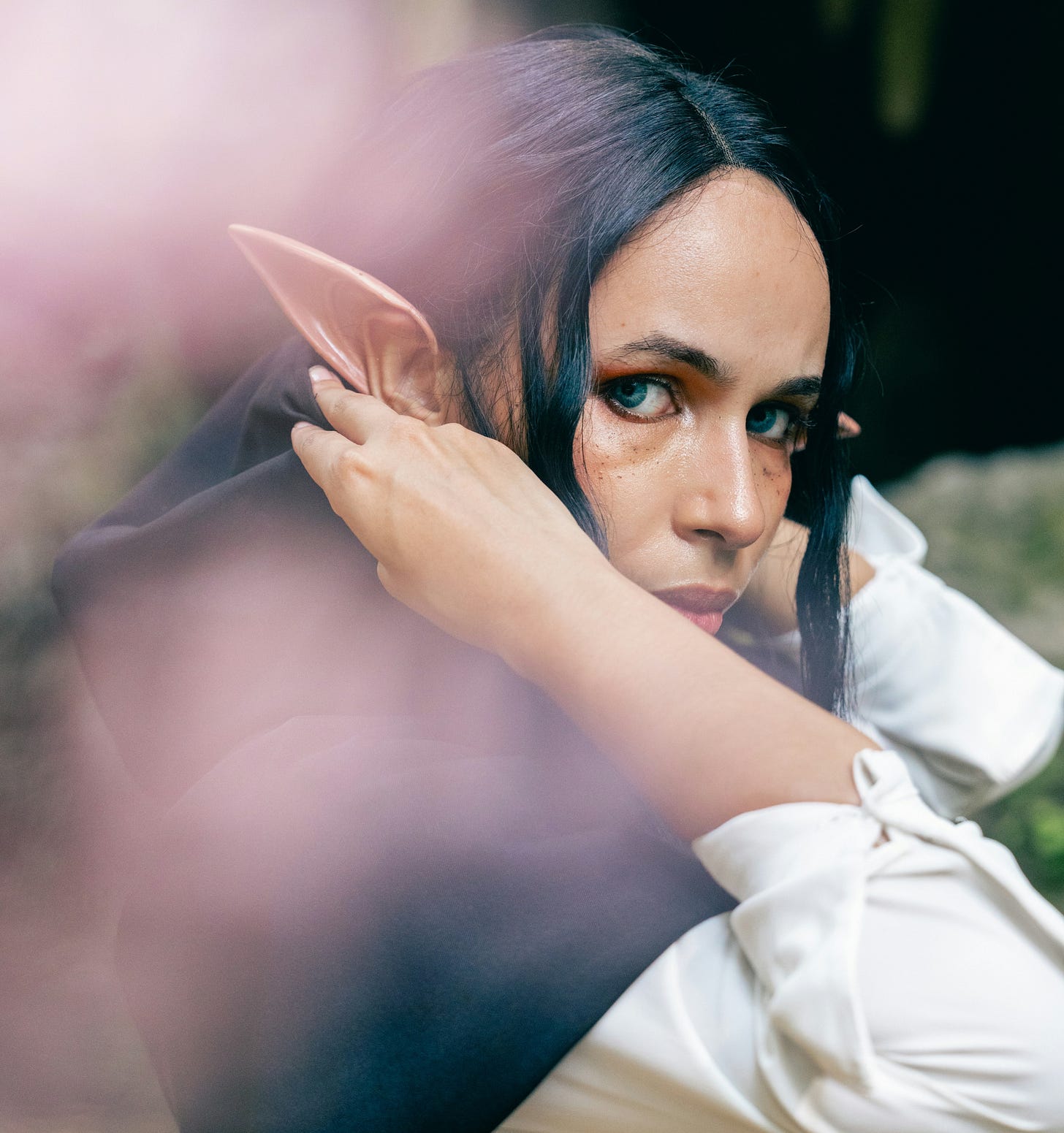 an elven woman with black hair pulls a hood over her head.