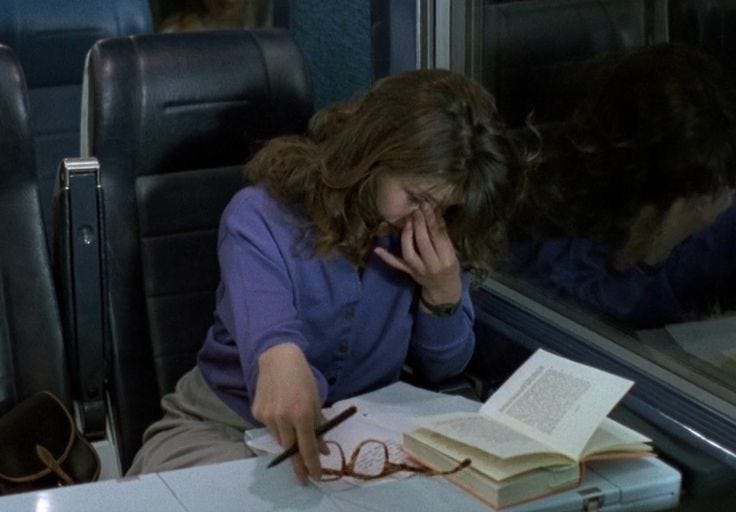 This may contain: a woman sitting at a table with an open book on her lap while talking on the phone