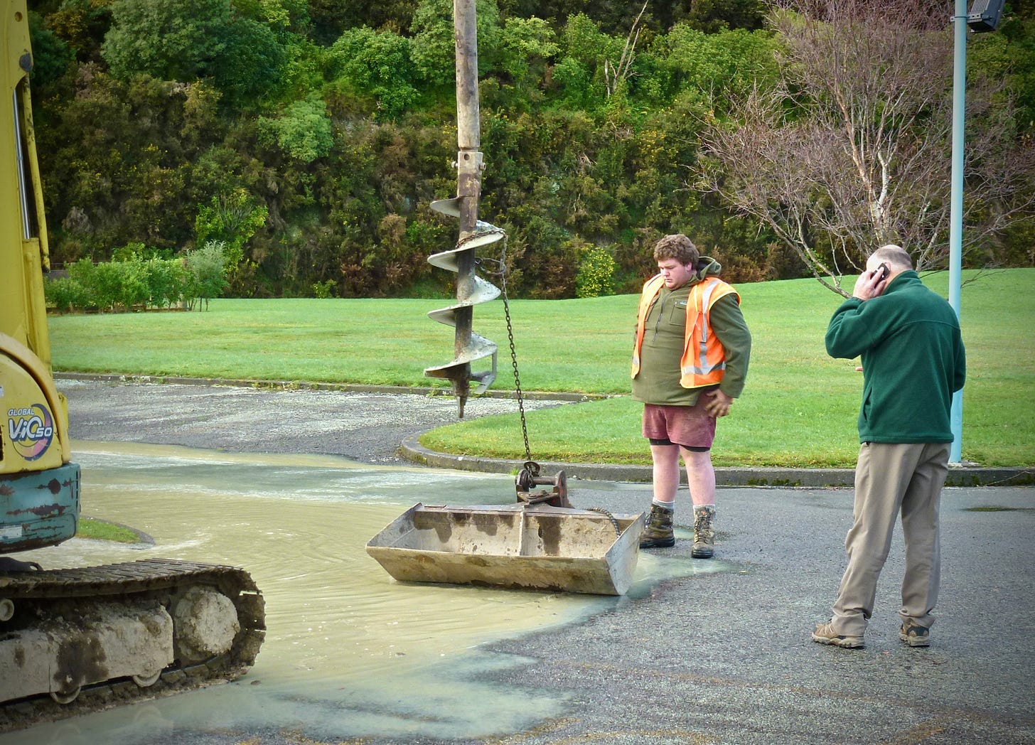 Machinery has drilled into a water main. A worker looks on forlornly while a manager makes a phone call.