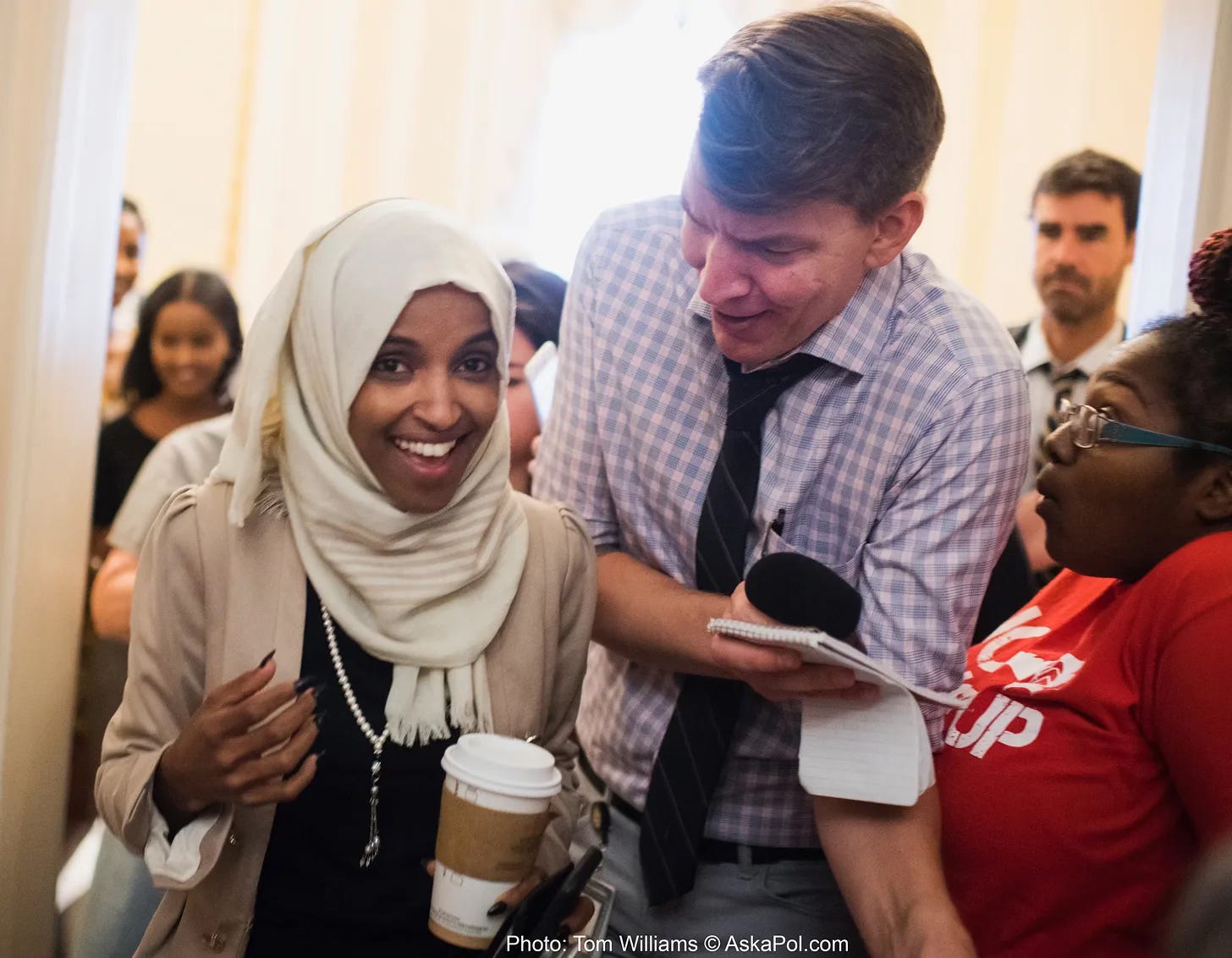 A Muslim Congresswoman holding a coffee cup is interviewed by tall white guy in middle of tourists at Capitol Photo: Tom Williams © www.thelcb.com A Muslim Congresswoman holding a coffee cup is interviewed by tall white guy in middle of tourists at Capitol Photo: Tom Williams © www.thelcb.com