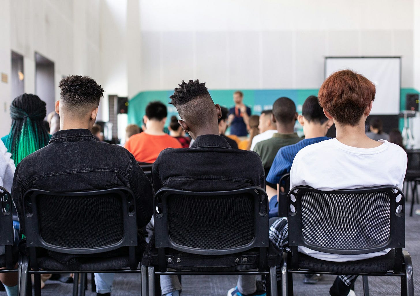 Three boys sitting in the back row of a classroom facing away from the camera.