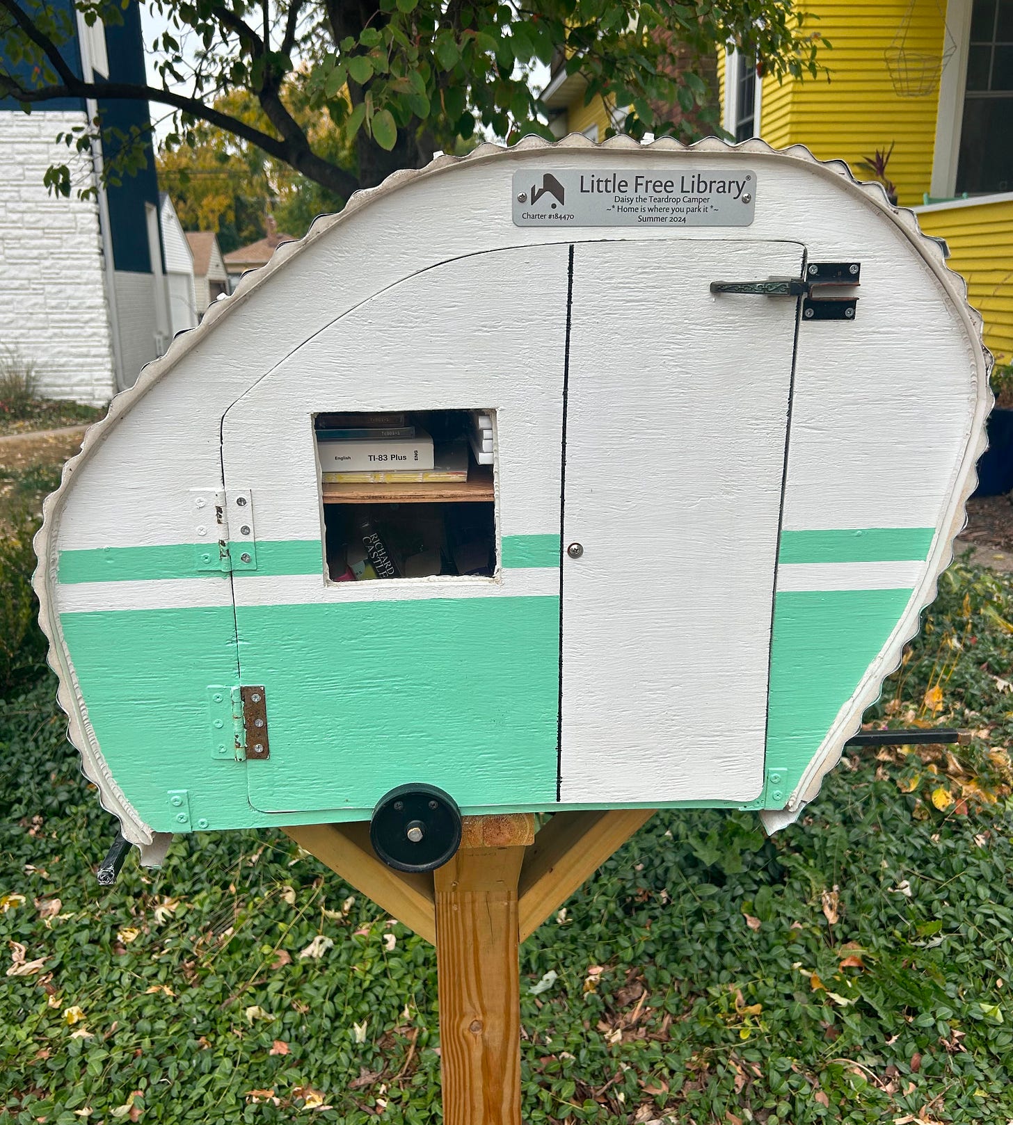 A little free library shaped like an RV trailer with mint trim