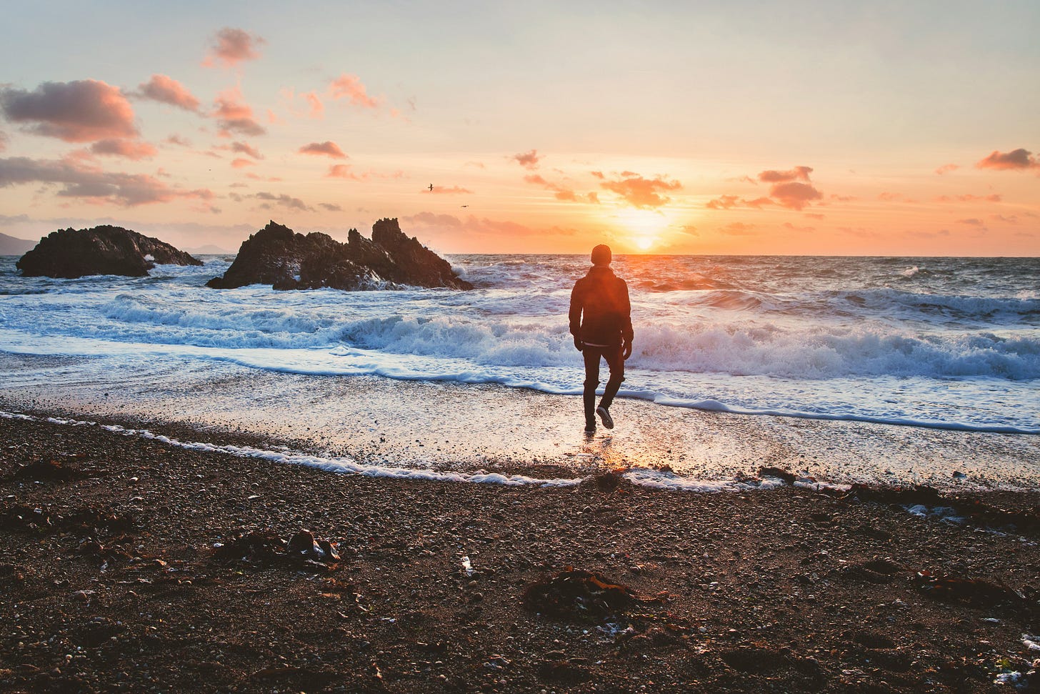 Image of a man walking on a beach at sunrise.