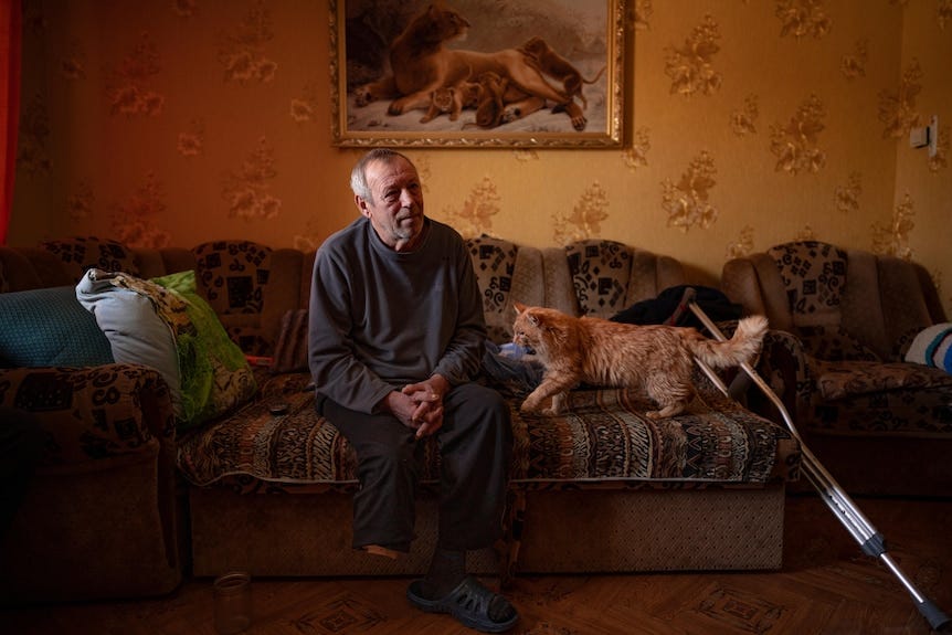 Oleksandr Rabenko sits on a coach next to his orange cat and his crutches Oleksandr Rabenko sits on a coach next to his orange cat and his crutches