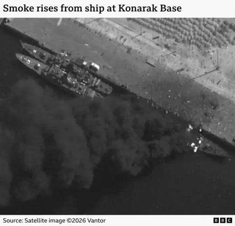 Three ships are seen docked at an Iranian port in a satellite image. Smoke can be seen billowing from one of the ships. The image is captioned "Smoke rises from ship at Konarak Base. Three ships are seen docked at an Iranian port in a satellite image. Smoke can be seen billowing from one of the ships. The image is captioned "Smoke rises from ship at Konarak Base.
