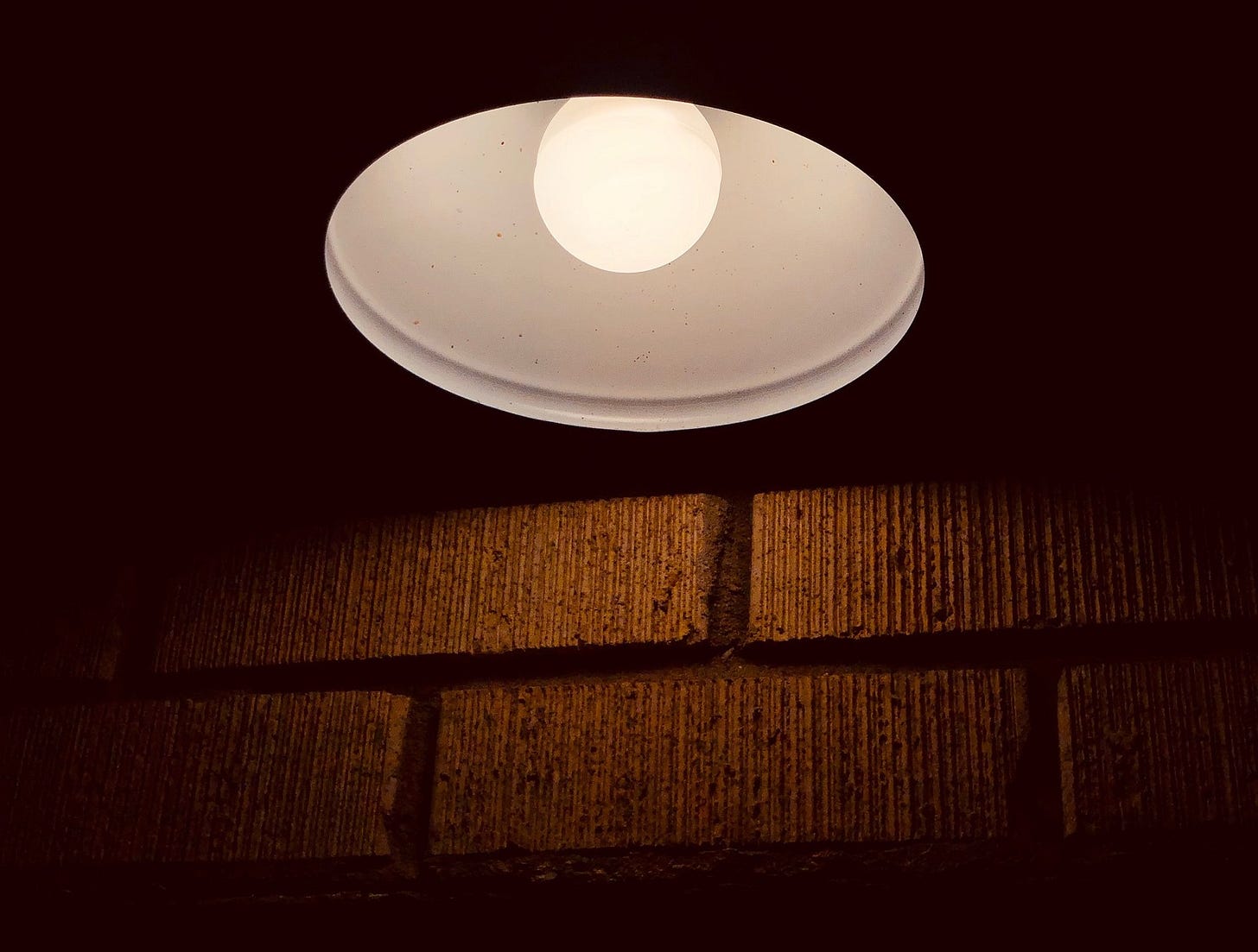 A porch light with a single light bulb shining at night A porch light with a single light bulb shining at night