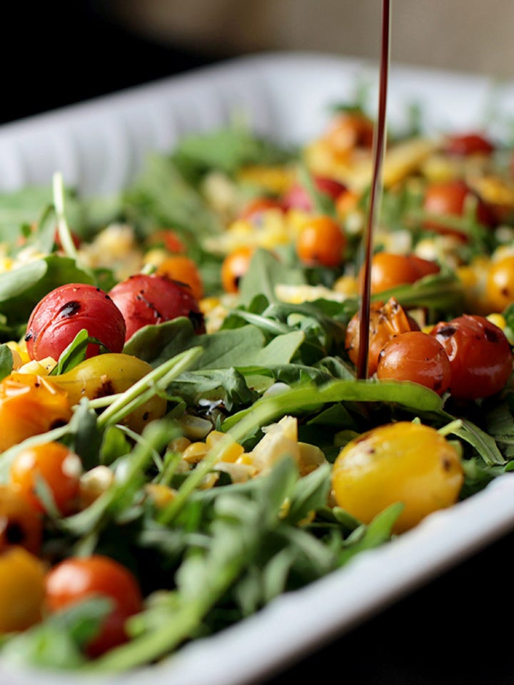 Blistered corn, tomato and arugula salad on white plates.