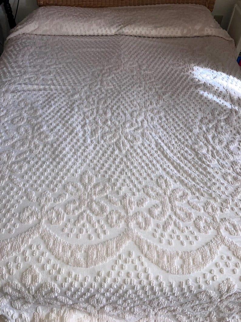 May include: A white, textured bedspread with a raised, embossed pattern. The pattern is a repeating design of small circles and floral shapes.