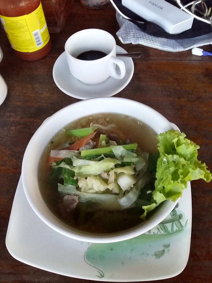 A collage of four food photographs arranged in a 2x2 grid. Top-left: A green ceramic mug filled with coffee featuring leaf-patterned latte art. Top-right: A hand holding a small plastic cup filled with a local sweet dessert topped with fresh shredded coconut. Bottom-left: A hearty bowl of clear broth soup filled with meat and green vegetables, sitting next to a white cup of black coffee. Bottom-right: A simple, rustic meal featuring a plate of white rice next to a small floral plate of meat stewed with ginger and local herbs.