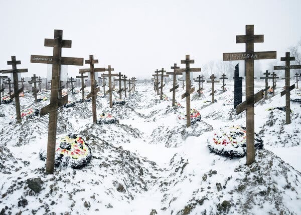 Lines of wooden crosses, placed atop grave mounds, stretch to the horizon in a snowy field.
