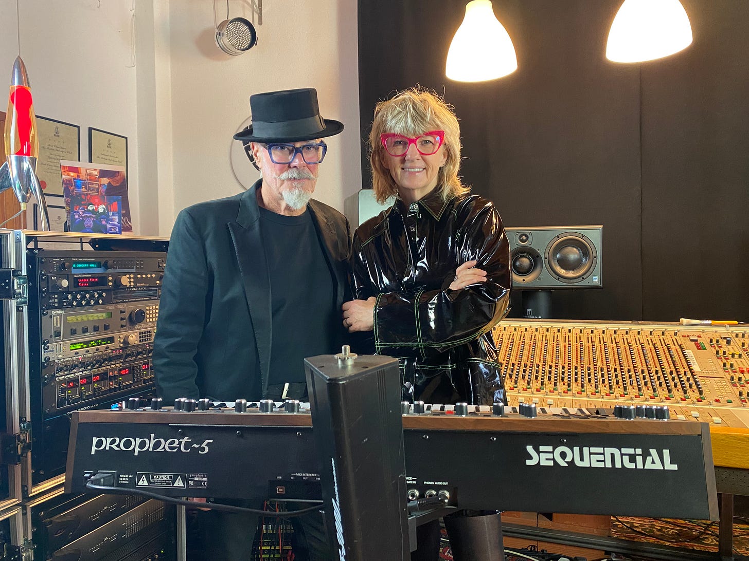 A man wearing a hat and glasses, a woman wering glasses - in a recording studio 
