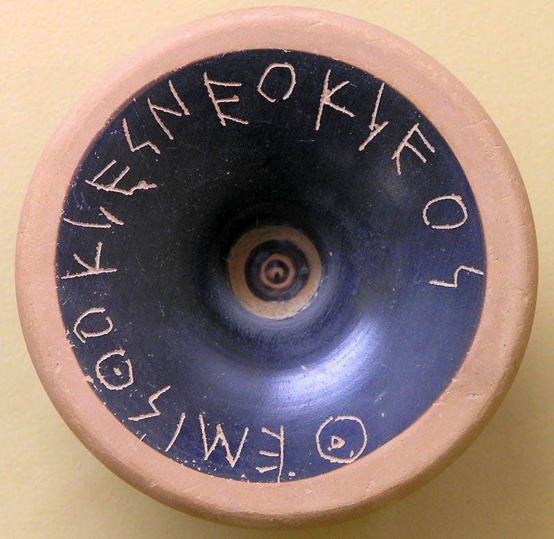 A round, orange and black piece of clay, on which Themistocles is scratched in Ancient Greek. A round, orange and black piece of clay, on which Themistocles is scratched in Ancient Greek.