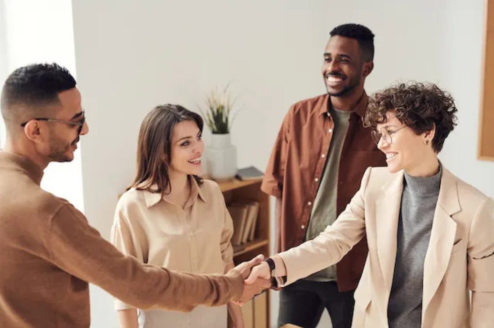 two people shake hands, smiling, while another two people look on