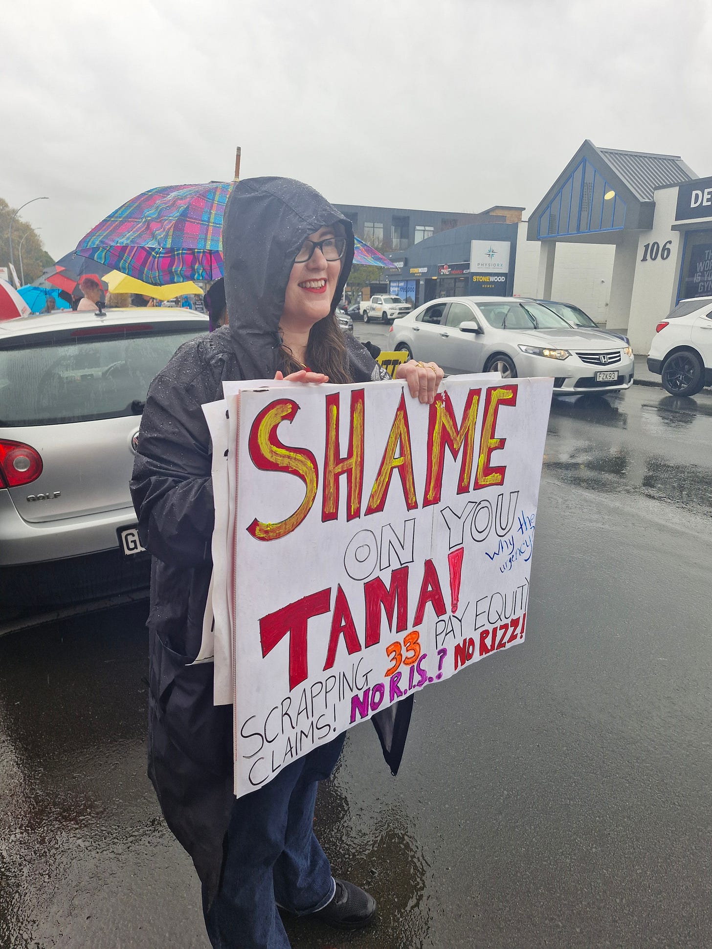 sign text reads: shame on you Tama! Scrapping 33 pay equity claims. NO R.I.S? NO RIZZ!!