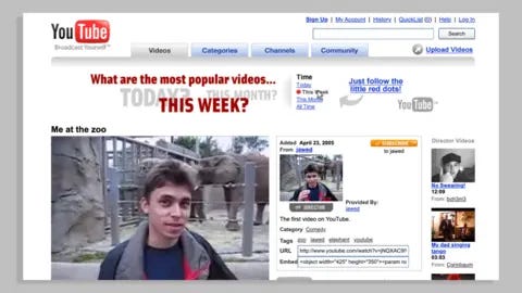 V&A An early YouTube watchpage. The red and black YouTube logo is seen against a white web page background. The page features an image of Jawed Karim from his video 'Me at the Zoo'. Kawed is a young man with dark hair and is pictured standing in front of an elephant enclosure.
