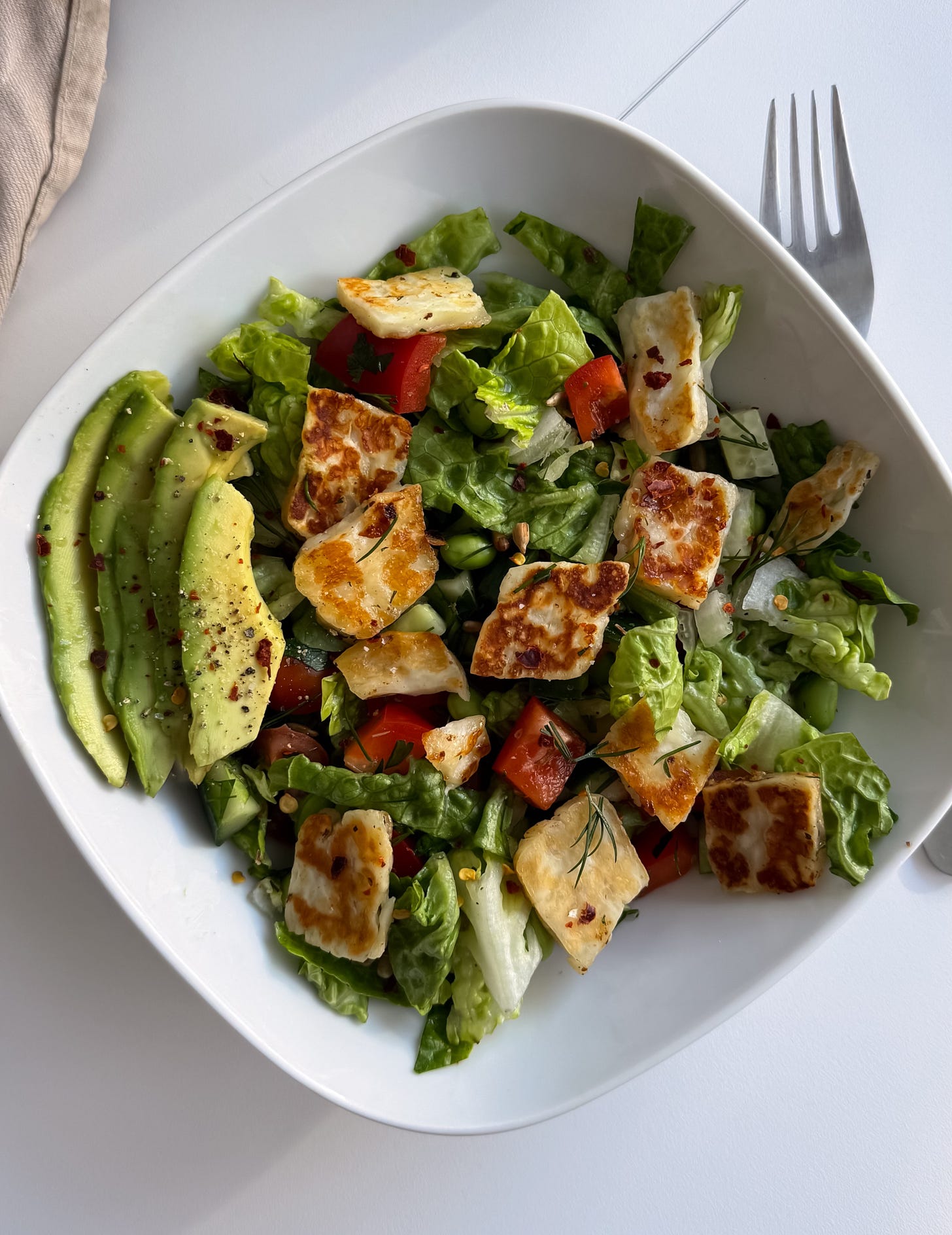 Top-down view of a colorful salad bowl with sliced avocado, hot honey-glazed halloumi, and fresh vegetables on a light background