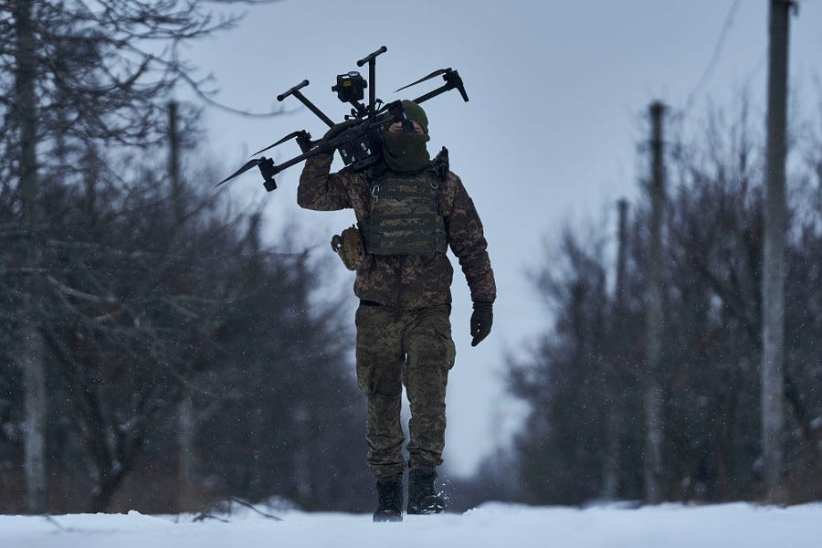 A soldier carries a drone on their shoulder while walking on a snow-covered road. A soldier carries a drone on their shoulder while walking on a snow-covered road.