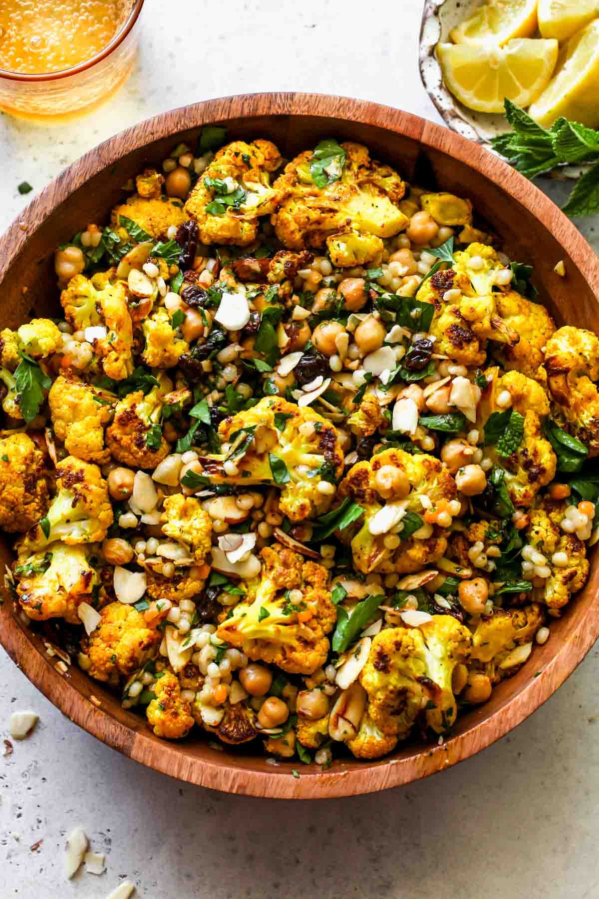 Moroccan cauliflower and couscous salad in a wooden serving bowl topped with herbs