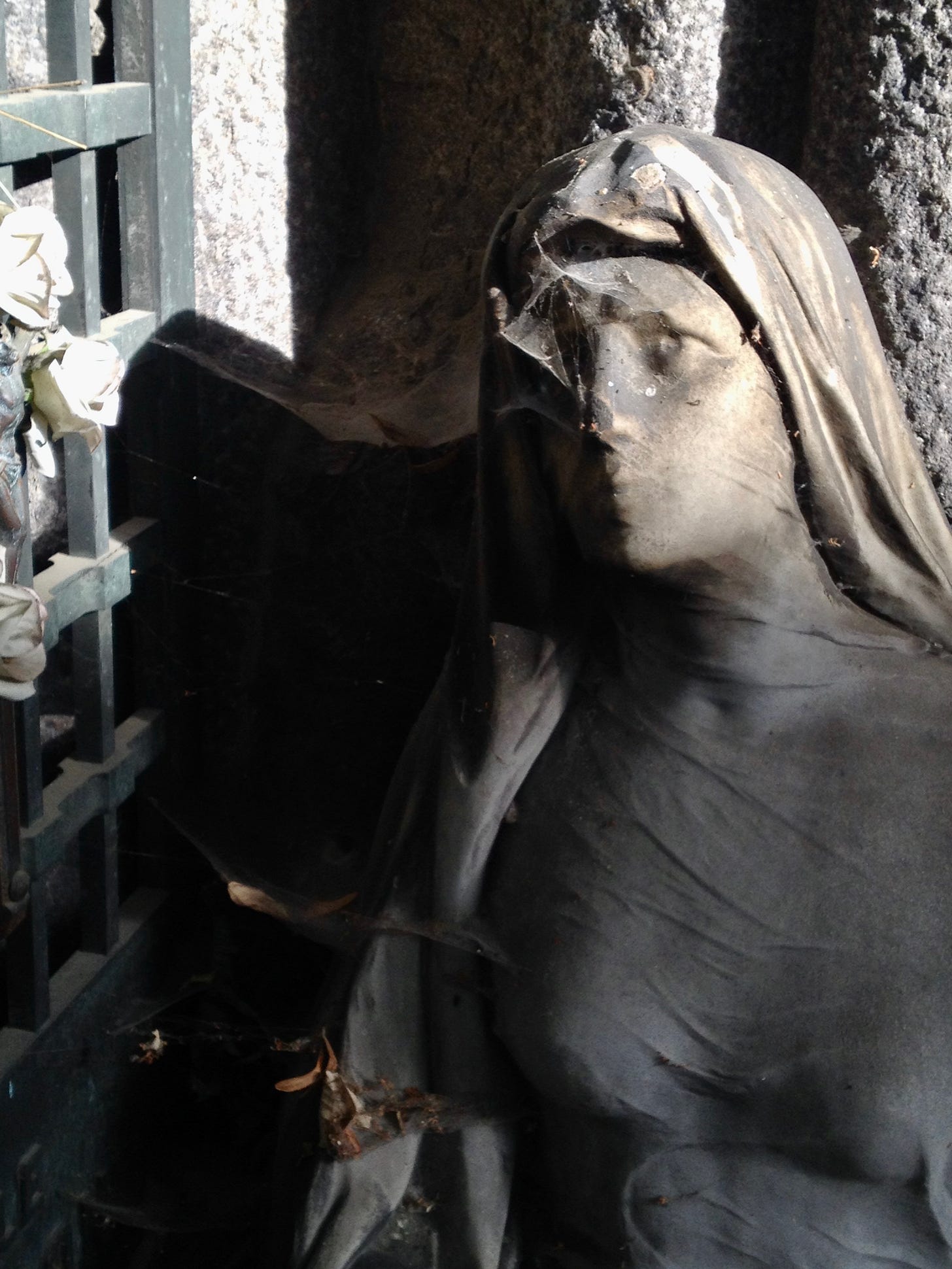 Weiblich gelesene Steinstatue auf einem Friedhof mit Spinnenweben im Gesicht