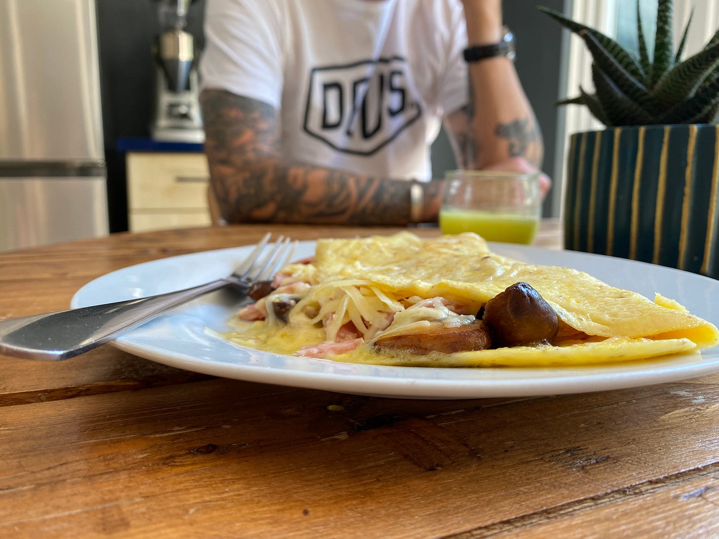 White plate with an omelette on, pieces of mushroom, ham and cheese are poking out from between the folded omelette
