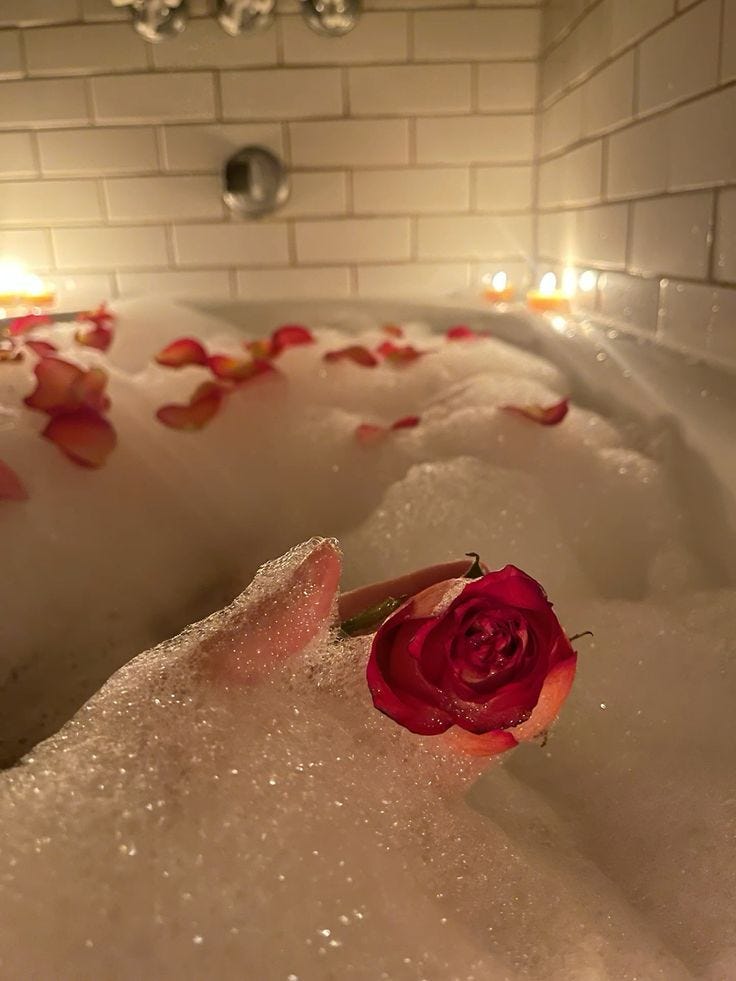 This may contain: a rose sitting in the middle of a bathtub filled with bubbles and water next to candles