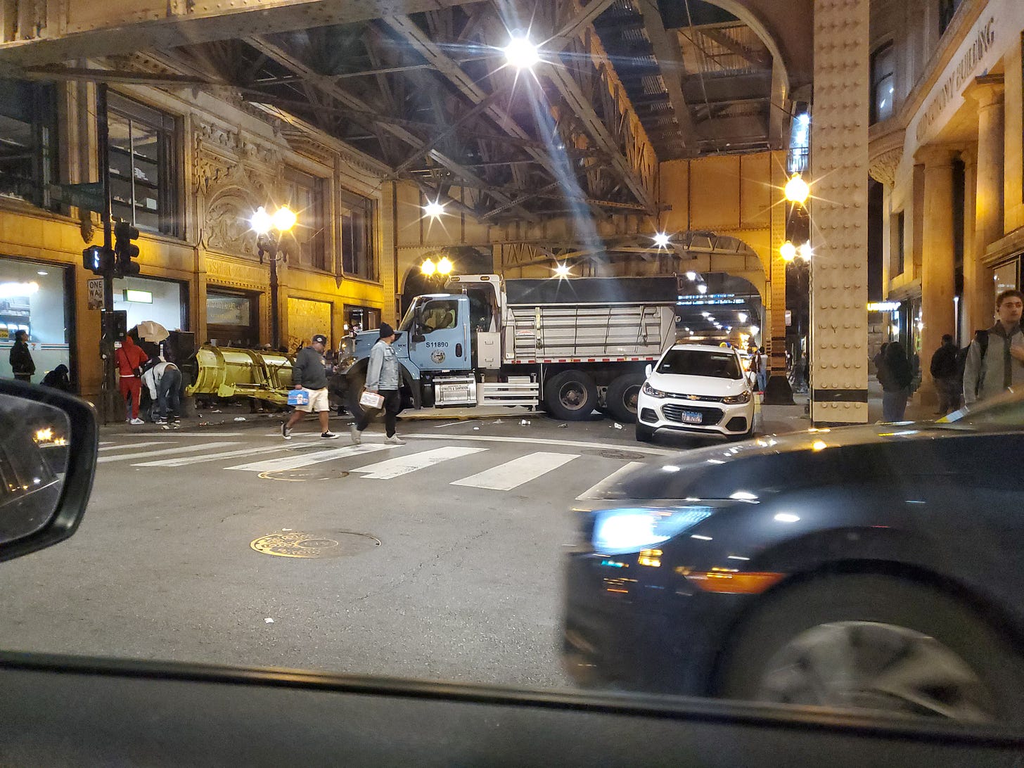 Van Buren Street in Chicago blocked with a snow plow to make way for the parade. Passersby with cases of beer using the crosswalk. 
