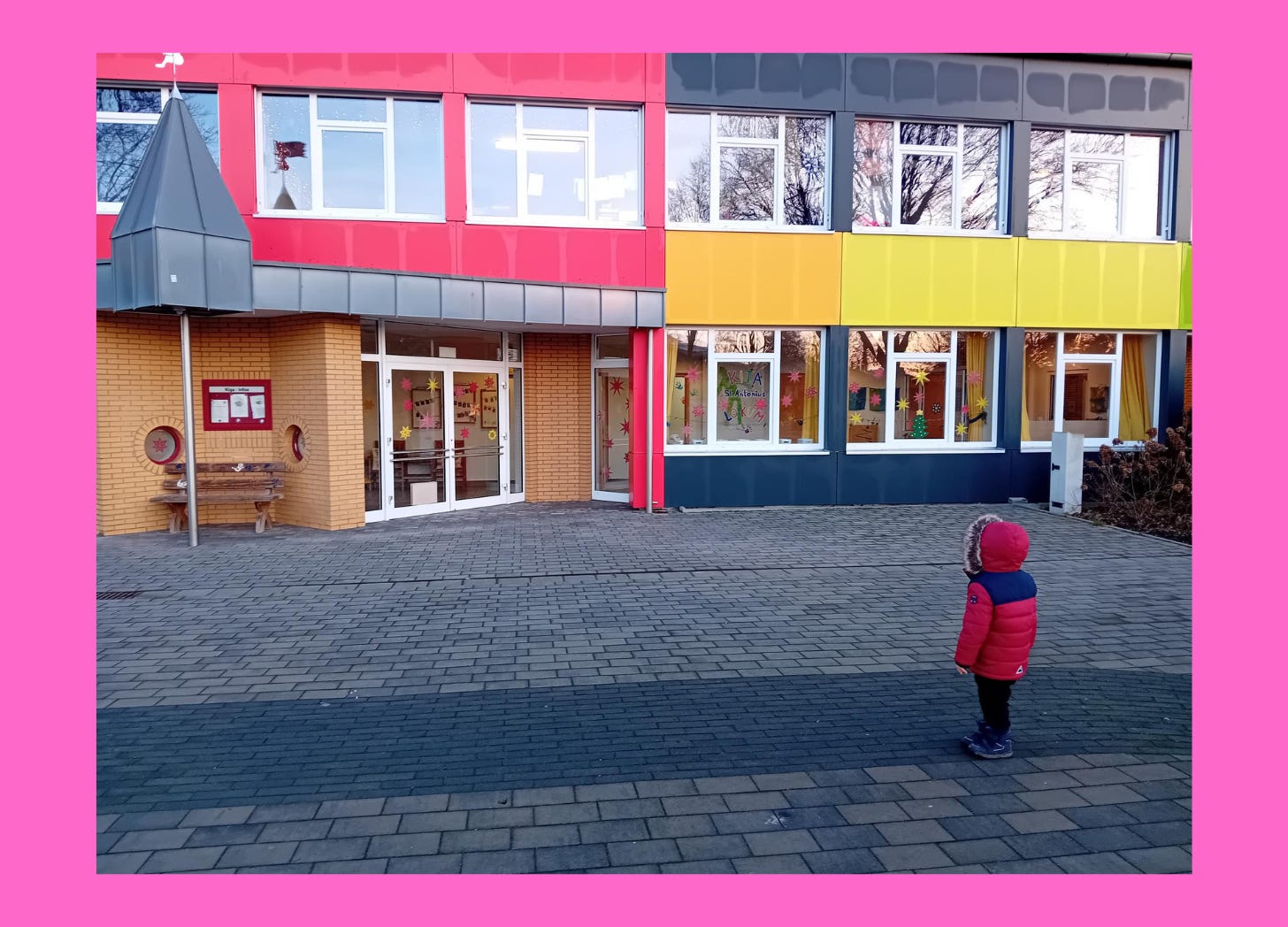 Photo of a small child in a winter coat in front of a school building.