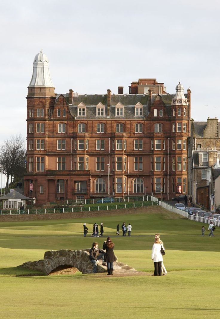 This may contain: people standing in front of a large building on a grass covered field next to a stone bridge This may contain: people standing in front of a large building on a grass covered field next to a stone bridge