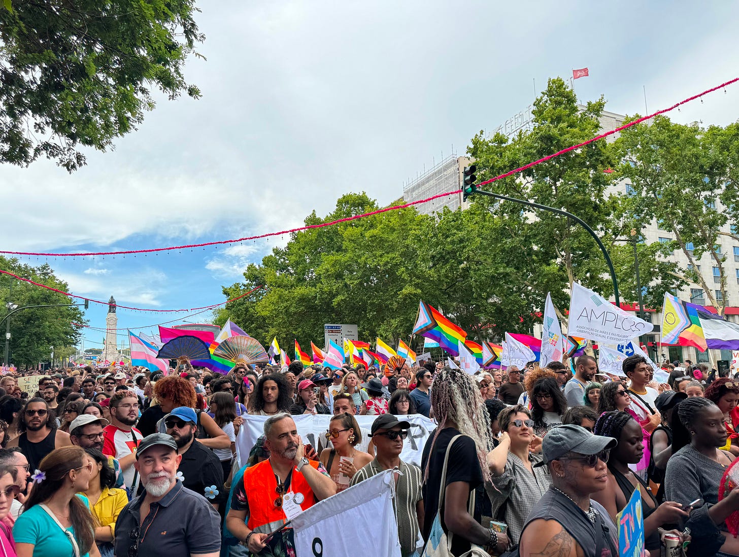 Variations of the rainbow flag fly above a crowd, with a historic statue in the background. Variations of the rainbow flag fly above a crowd, with a historic statue in the background.